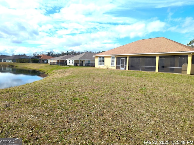 back of property featuring a sunroom, a water view, and a yard