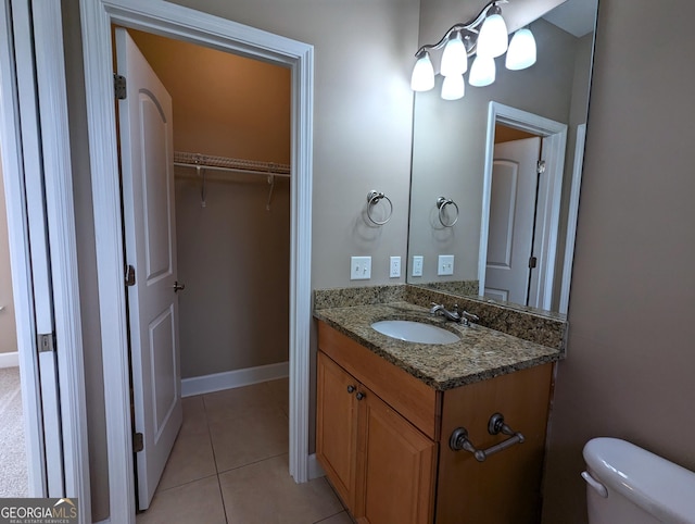 half bathroom with baseboards, toilet, tile patterned floors, a walk in closet, and vanity