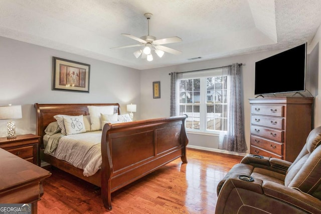 bedroom with visible vents, baseboards, a ceiling fan, wood finished floors, and a textured ceiling