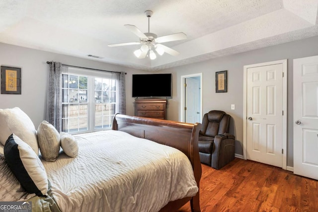 bedroom featuring a raised ceiling, visible vents, dark wood-type flooring, a textured ceiling, and baseboards