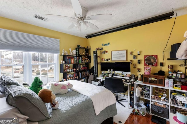 bedroom with a ceiling fan, visible vents, a textured ceiling, and wood finished floors