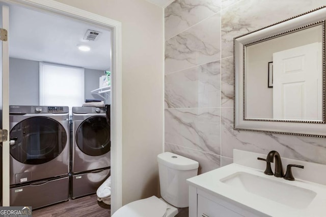 bathroom featuring toilet, separate washer and dryer, vanity, visible vents, and tile walls