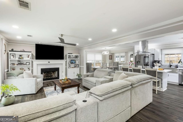 living area featuring visible vents, a tiled fireplace, ornamental molding, dark wood-type flooring, and recessed lighting