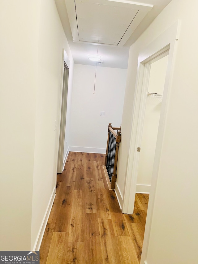 hall featuring attic access, light wood-style flooring, and baseboards