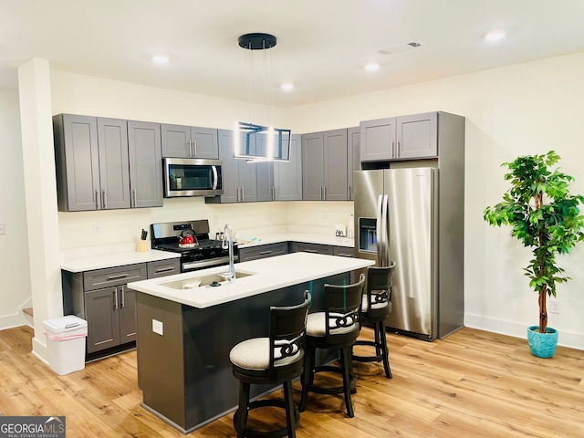 kitchen featuring a breakfast bar area, stainless steel appliances, light countertops, light wood-style floors, and a kitchen island with sink