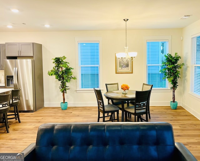 dining room with baseboards, light wood finished floors, visible vents, and an inviting chandelier