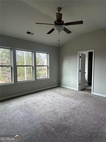 carpeted empty room featuring lofted ceiling, visible vents, baseboards, and a ceiling fan