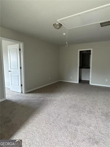 carpeted spare room featuring attic access, visible vents, and baseboards