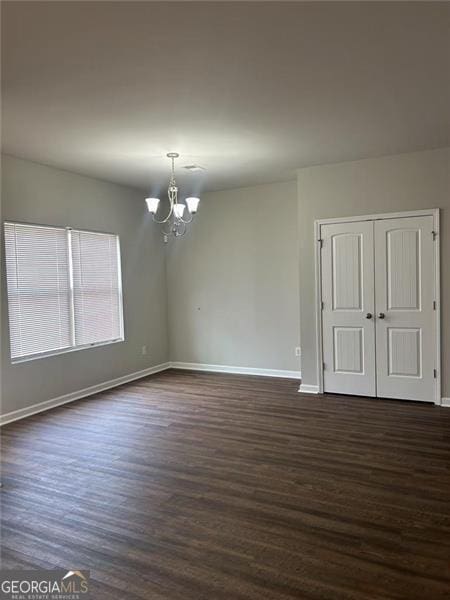 spare room with a notable chandelier, dark wood-type flooring, and baseboards