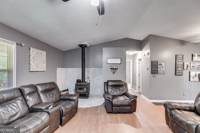 living room featuring lofted ceiling, a wood stove, ceiling fan, and light wood finished floors