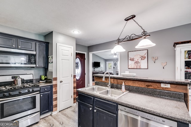 kitchen with appliances with stainless steel finishes, a sink, decorative light fixtures, and dark cabinetry