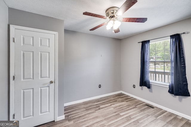 spare room with a textured ceiling, baseboards, visible vents, and light wood-style floors