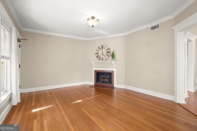 unfurnished living room with a fireplace, wood finished floors, visible vents, baseboards, and ornamental molding