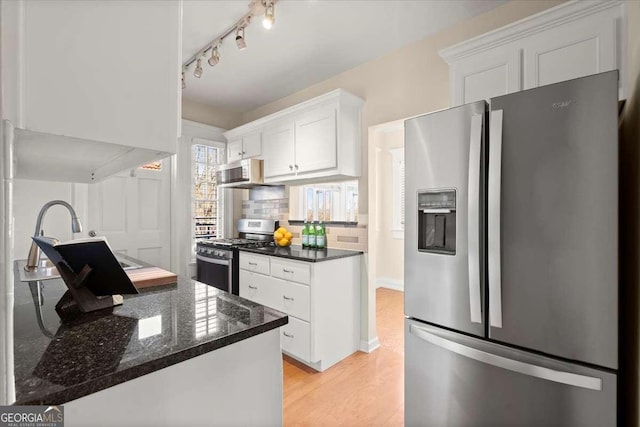 kitchen featuring stainless steel appliances, light wood-style floors, white cabinets, tasteful backsplash, and dark stone countertops