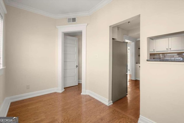 corridor with ornamental molding, wood finished floors, visible vents, and baseboards