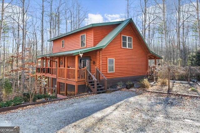 view of front of property featuring covered porch, driveway, log exterior, and metal roof