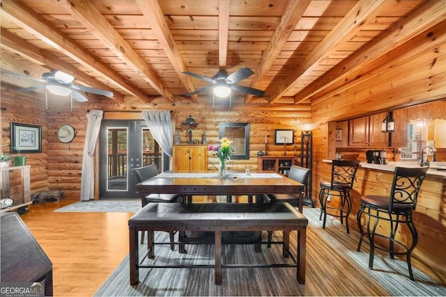 dining area featuring light wood-style floors, wood ceiling, rustic walls, and beamed ceiling