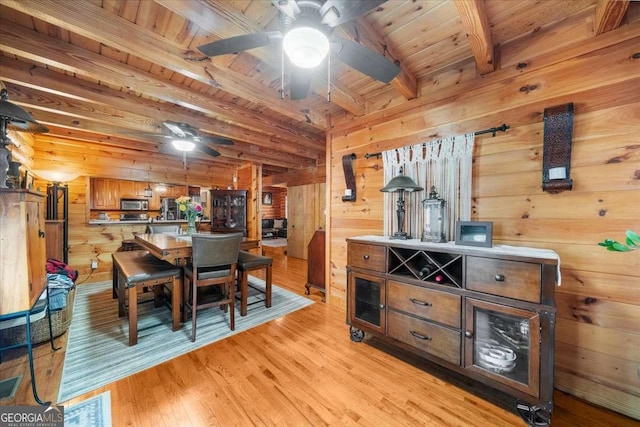 dining room with light wood-style flooring, wooden walls, a ceiling fan, wood ceiling, and beam ceiling