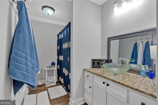 full bath featuring a textured ceiling, wood finished floors, vanity, baseboards, and ornamental molding