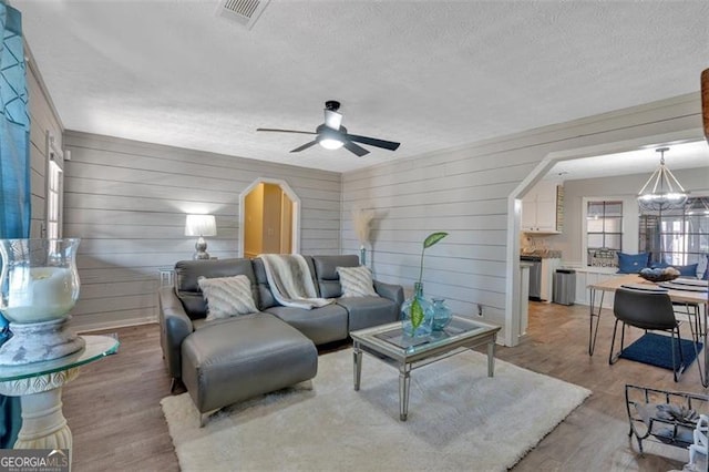 living room with a textured ceiling, ceiling fan with notable chandelier, visible vents, and light wood-style floors