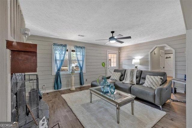 living room with a ceiling fan, a textured ceiling, arched walkways, and wood finished floors