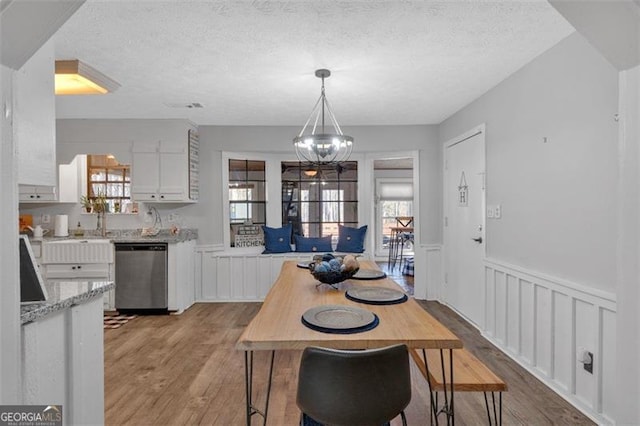 dining space featuring light wood finished floors, a decorative wall, an inviting chandelier, wainscoting, and a textured ceiling