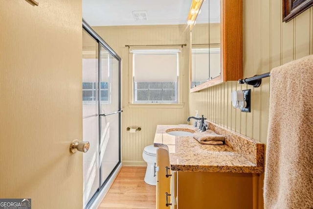 bathroom with a shower with door, toilet, wood walls, vanity, and wood finished floors