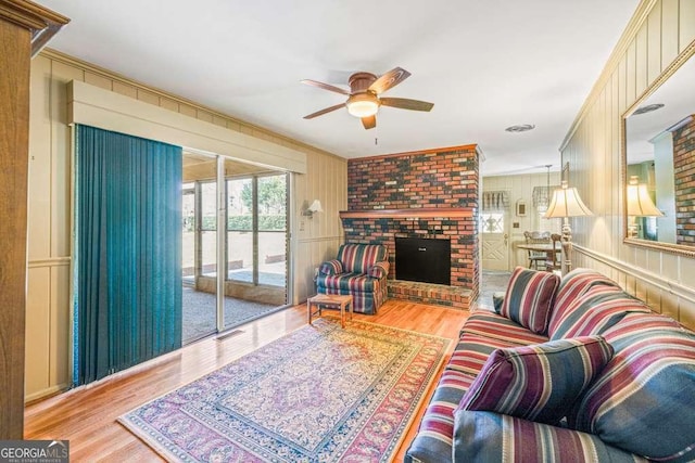 living area featuring light wood-style floors, a fireplace, a decorative wall, and a ceiling fan