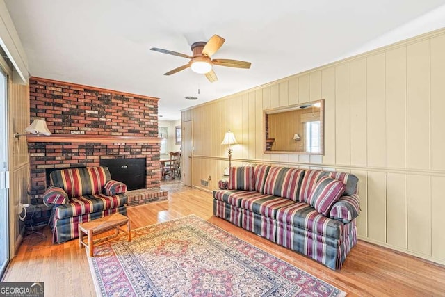 living room with ornamental molding, a brick fireplace, ceiling fan, and light wood finished floors