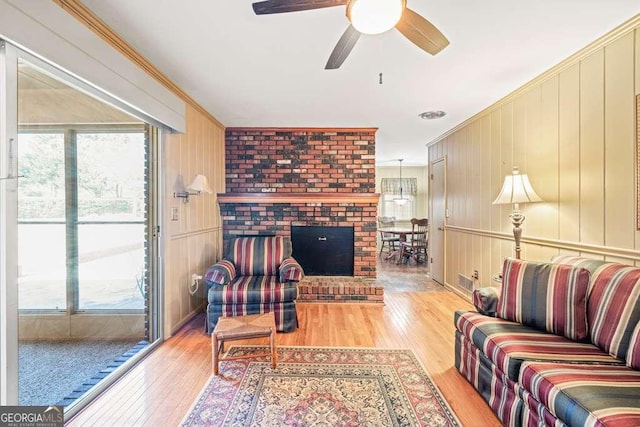 living area with light wood-style floors, a fireplace, ornamental molding, and a ceiling fan