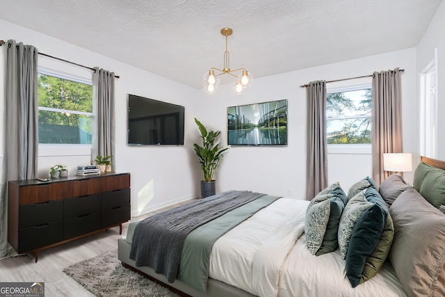 bedroom with a textured ceiling, multiple windows, an inviting chandelier, and light wood-style floors