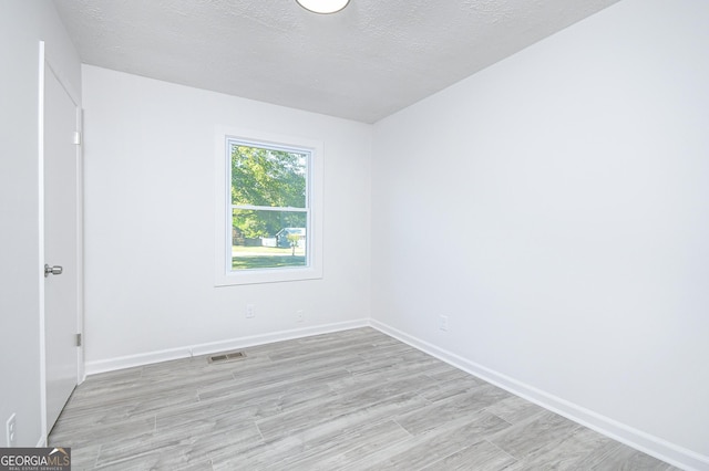 empty room with light wood-type flooring, visible vents, a textured ceiling, and baseboards