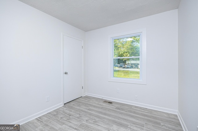 unfurnished room featuring light wood finished floors, baseboards, visible vents, and a textured ceiling