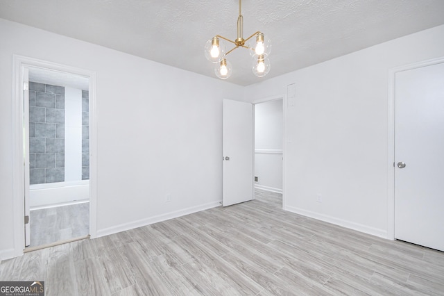 unfurnished room featuring baseboards, a textured ceiling, light wood finished floors, and an inviting chandelier