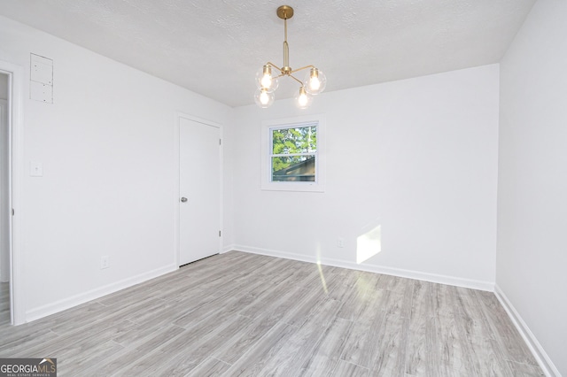 spare room featuring light wood-type flooring, an inviting chandelier, baseboards, and a textured ceiling