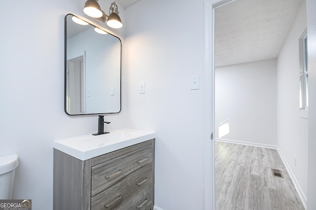 bathroom with toilet, wood finished floors, vanity, visible vents, and baseboards