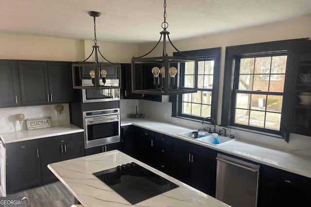 kitchen featuring pendant lighting, decorative backsplash, appliances with stainless steel finishes, a sink, and dark cabinetry