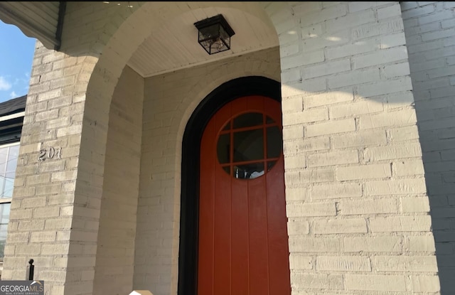 doorway to property with brick siding and roof with shingles