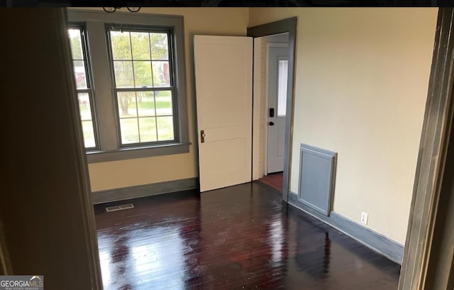 empty room with dark wood finished floors, visible vents, and baseboards