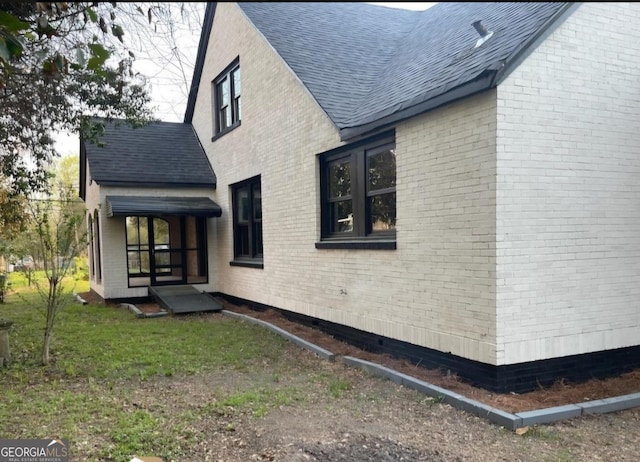 view of home's exterior with brick siding and roof with shingles