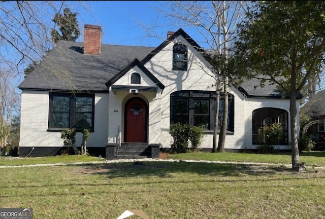 tudor house with entry steps, brick siding, and a front yard