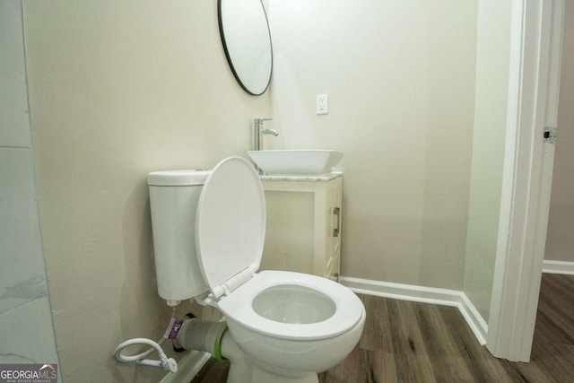 half bathroom featuring wood finished floors, a sink, toilet, and baseboards