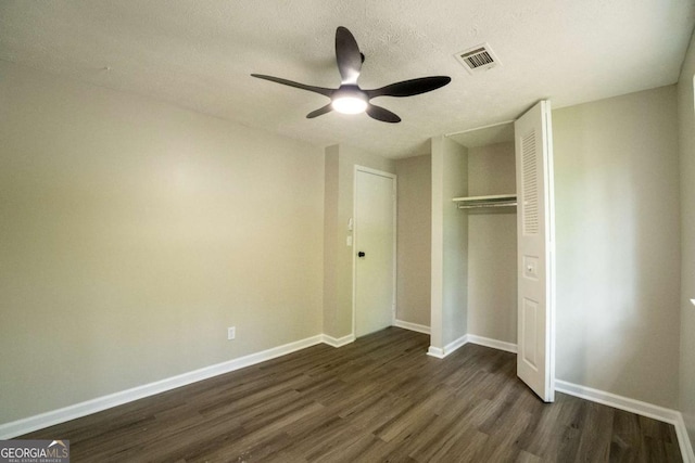 unfurnished bedroom with a textured ceiling, dark wood-style flooring, visible vents, baseboards, and a closet