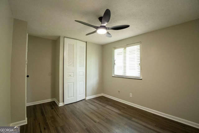 unfurnished bedroom with a textured ceiling, dark wood-style flooring, a closet, and baseboards