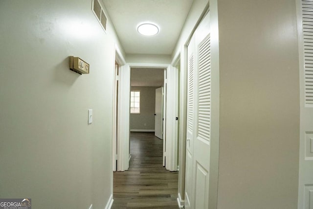 hallway featuring dark wood-type flooring, visible vents, and baseboards