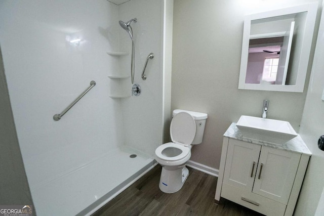 bathroom with toilet, a stall shower, vanity, wood finished floors, and baseboards