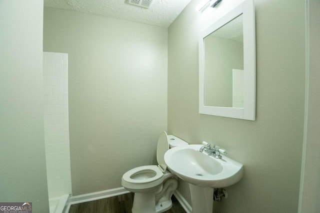 full bathroom with a textured ceiling, toilet, wood finished floors, visible vents, and baseboards