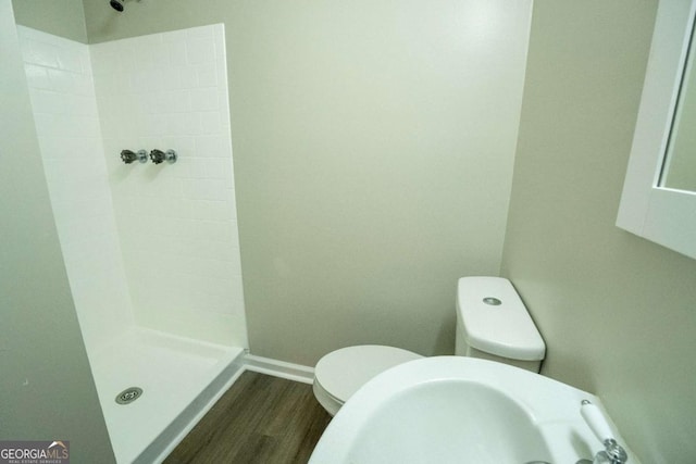 bathroom with toilet, a sink, a shower stall, wood finished floors, and baseboards