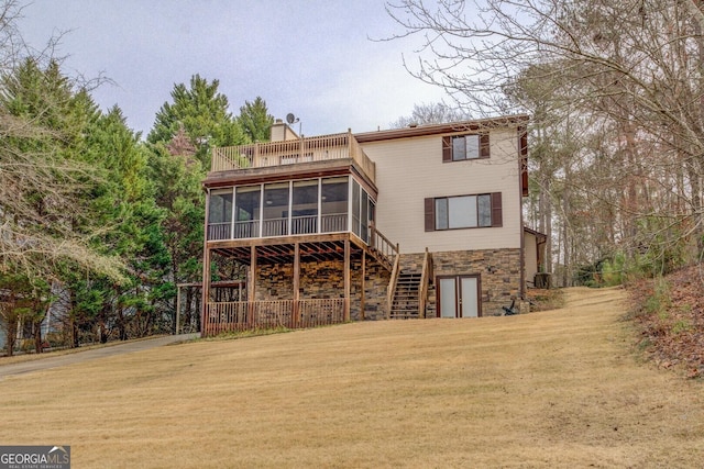 back of house with a sunroom, stairs, stone siding, a lawn, and a chimney