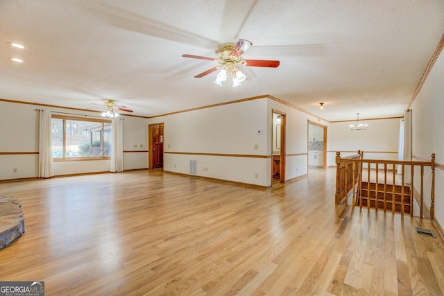 empty room with ornamental molding, light wood-type flooring, visible vents, and a textured ceiling